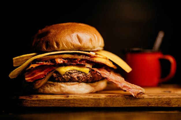 Hamburger s hovězím, se slaninou a sýrem na dřevěném prkénku.