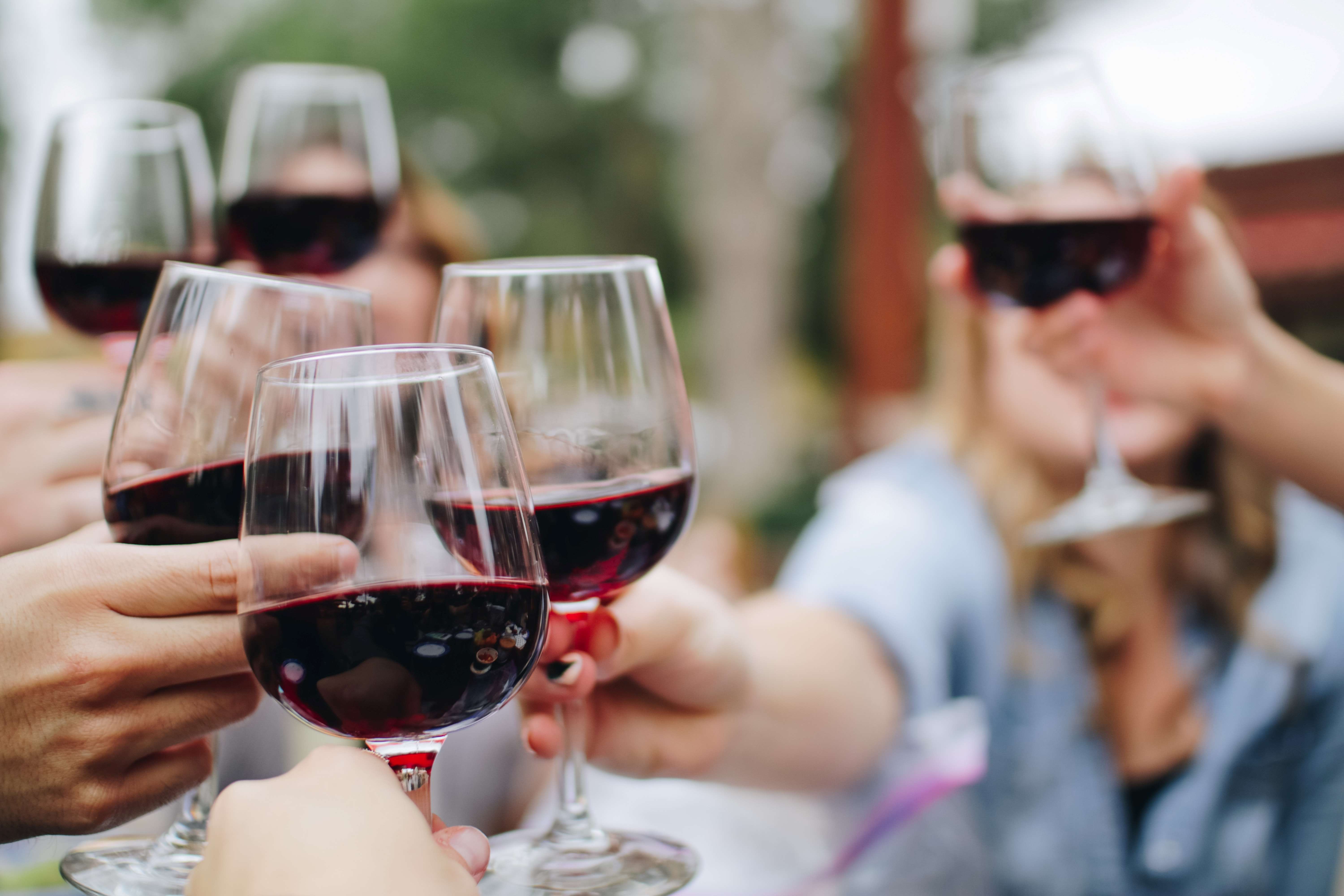 Společnost několika lidí, kteří si vzájemně přiťukávají sklenkou červeného vína