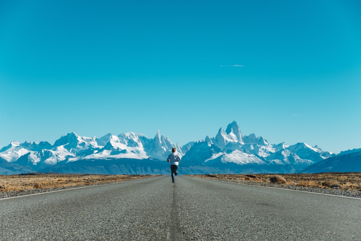 muž běžící po silnici a před ním zasněžené hory